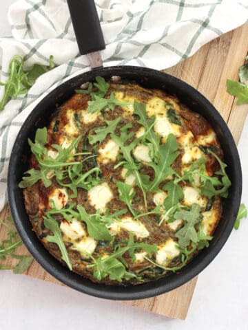 Mushrrom spinach goats cheese frittata in a black skillet on a wooden chopping board.