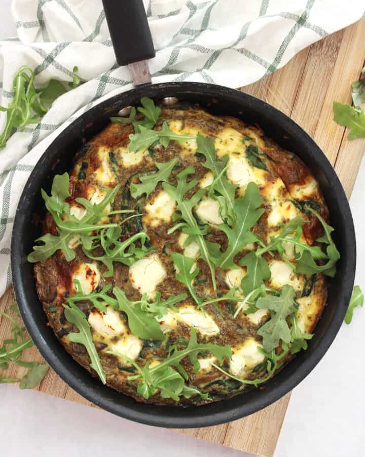 Mushrrom spinach goats cheese frittata in a black skillet on a wooden chopping board.