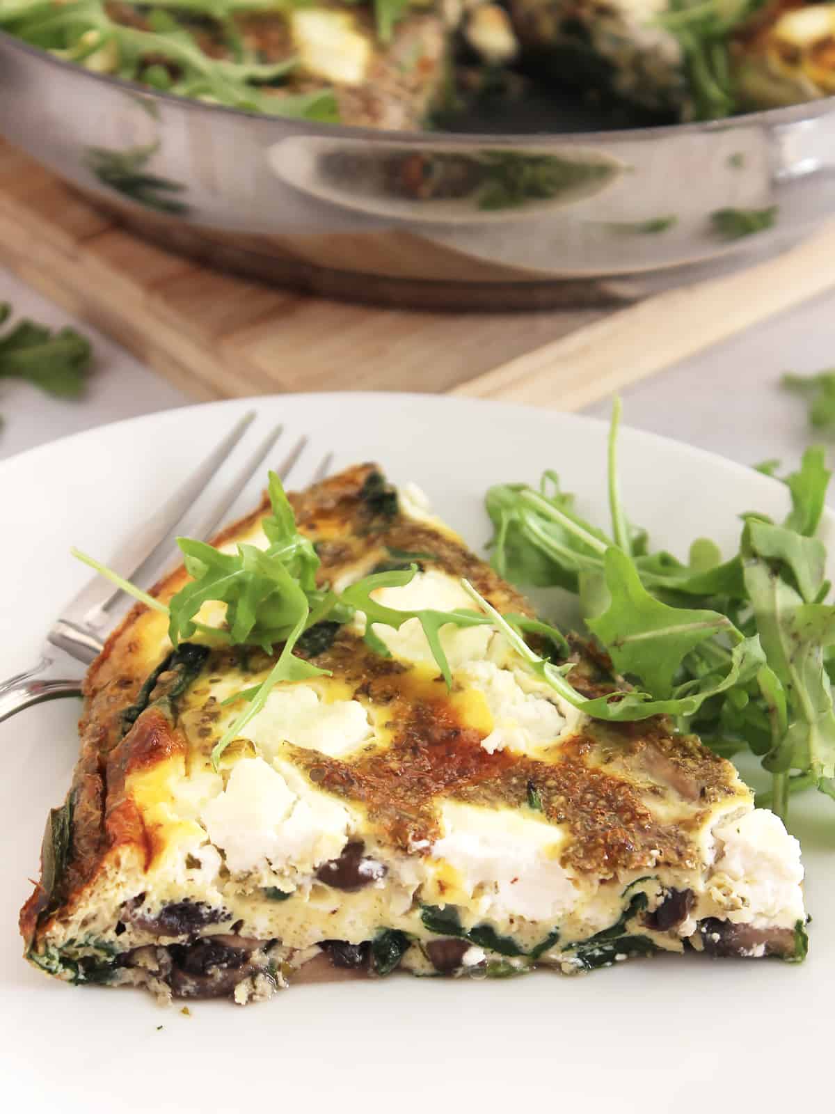 Close up of a slice of frittata on a plate with fresh arugula.