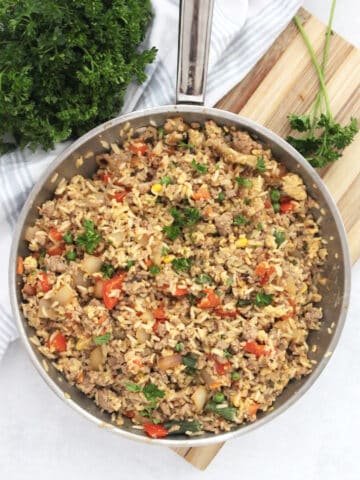 Overhead shot og ground turkey fried rice in a skillet on a chopping board, garnished with fresh parsley.