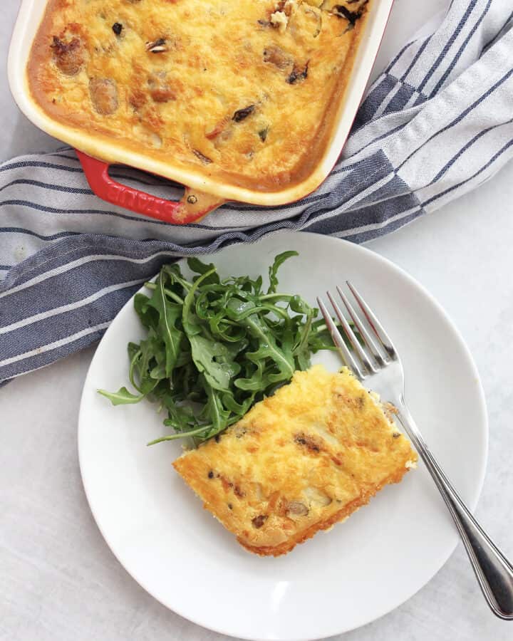 Overhead shot of an air fryer breakfast casserole in a baking dish and a piece served on a plate with a salad.