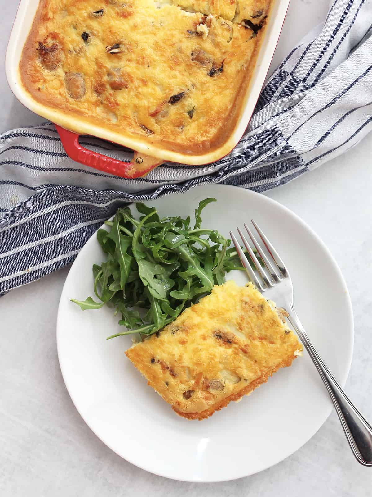 Overhead shot of an air fryer breakfast casserole in a baking dish and a piece served on a plate with a salad.