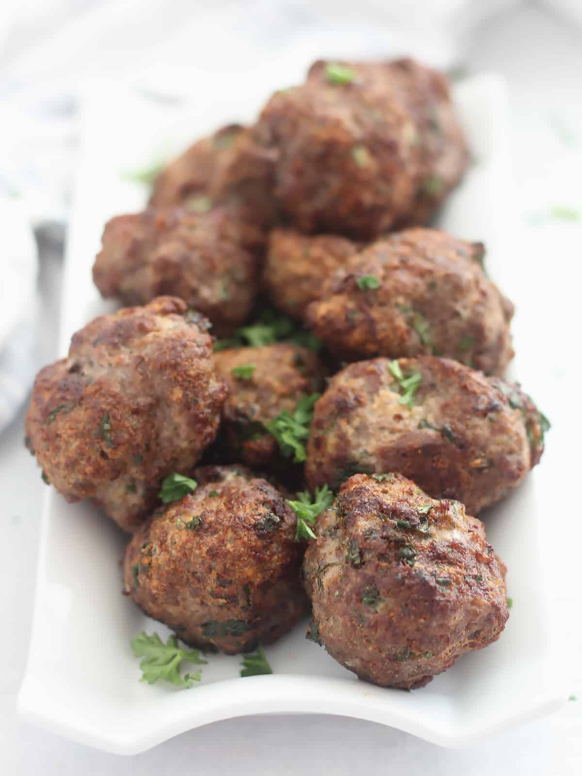 Air fried lamb meatballs on a white plate garnished with fresh parsley.