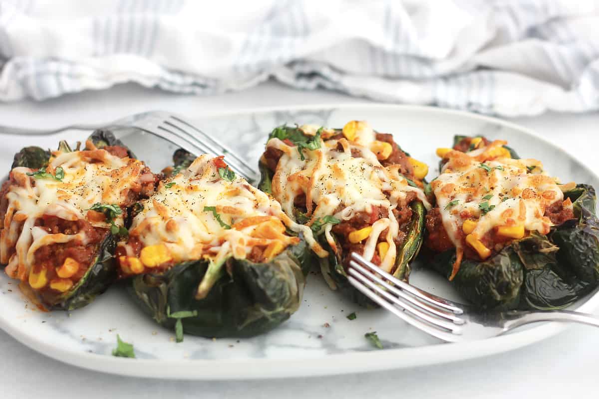 Four air fried stuffed poblano peppers on a serving plate with two forks.