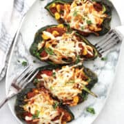 Four stuffed poblano pepper halves on a serving plate.