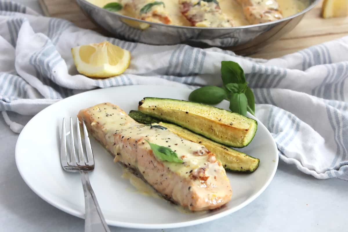 A fillet of salmon served on a plate with zucchini and topped with a creamy sauce.