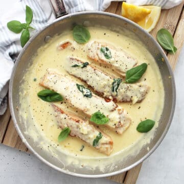 Salmon with lemon and basil sauce in a skillet garnished with fresh basil leaves.