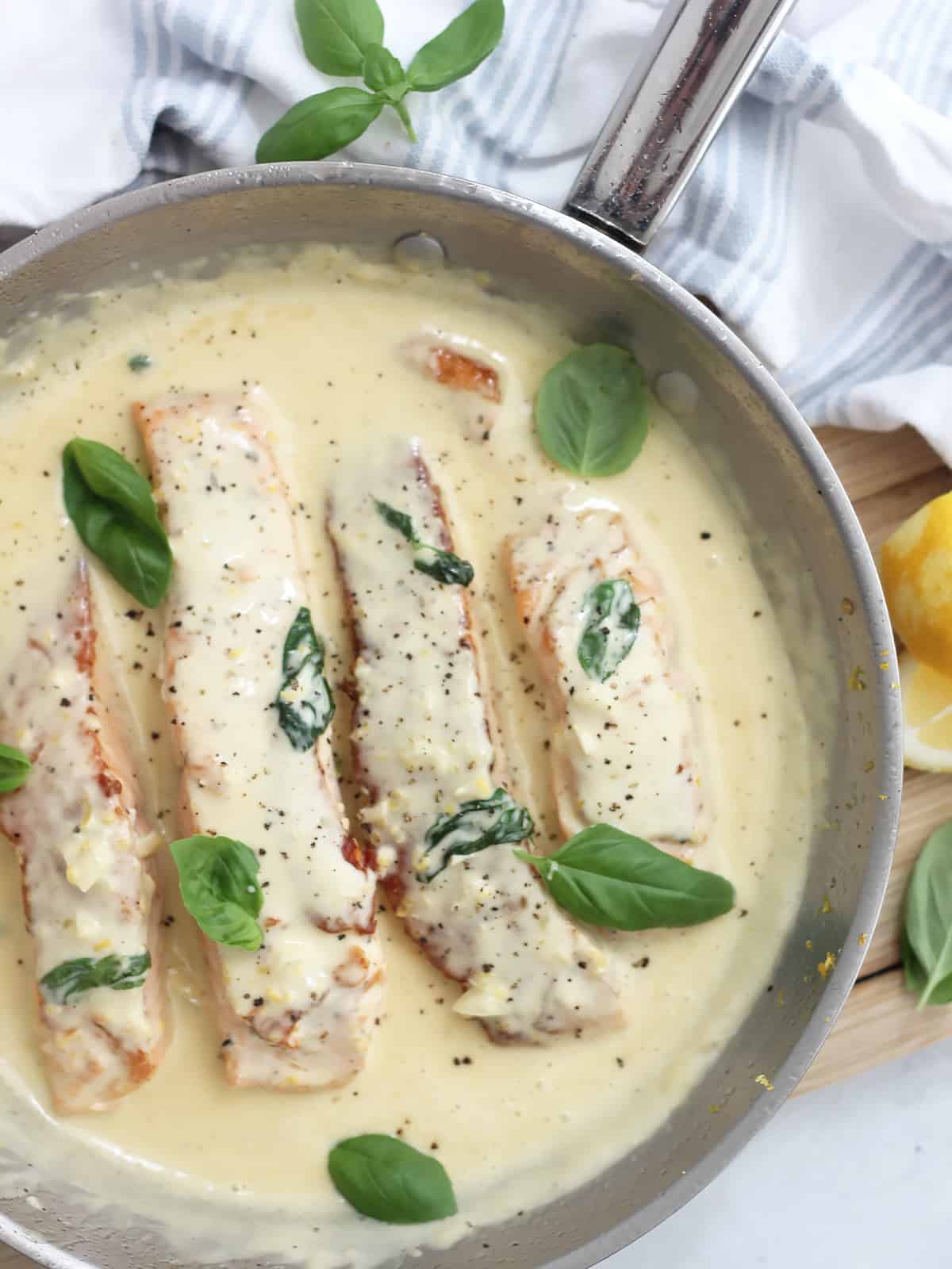 Salmon fillets in a skillet with a cream sauce spooned over the top.