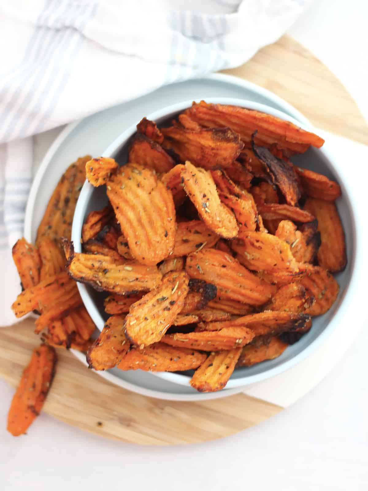 Overhead shot of air fried carrot chips in a bowl next to a cloth.
