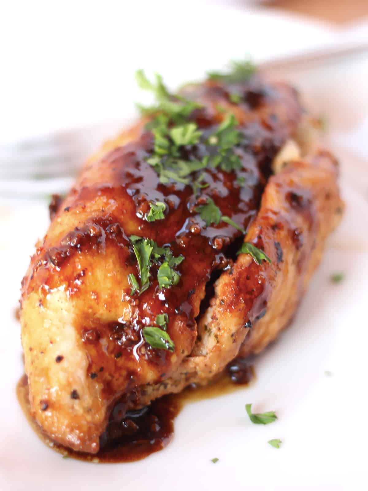 A stuffed chicken breast with balsamic reduction and fresh herb garnish.