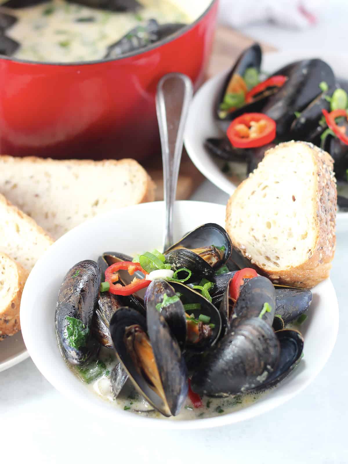 A bowl of mussels in coconut broth with a spoon and slice of bread.