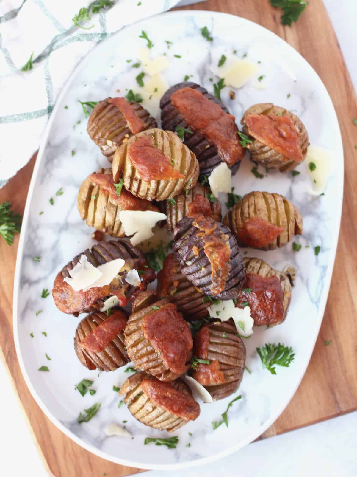 Mini hasselback potatoes on a serving plate topped with parmesan shavings and fresh herbs.