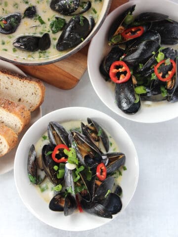Two bowls of mussels next to a plate of sliced bread.