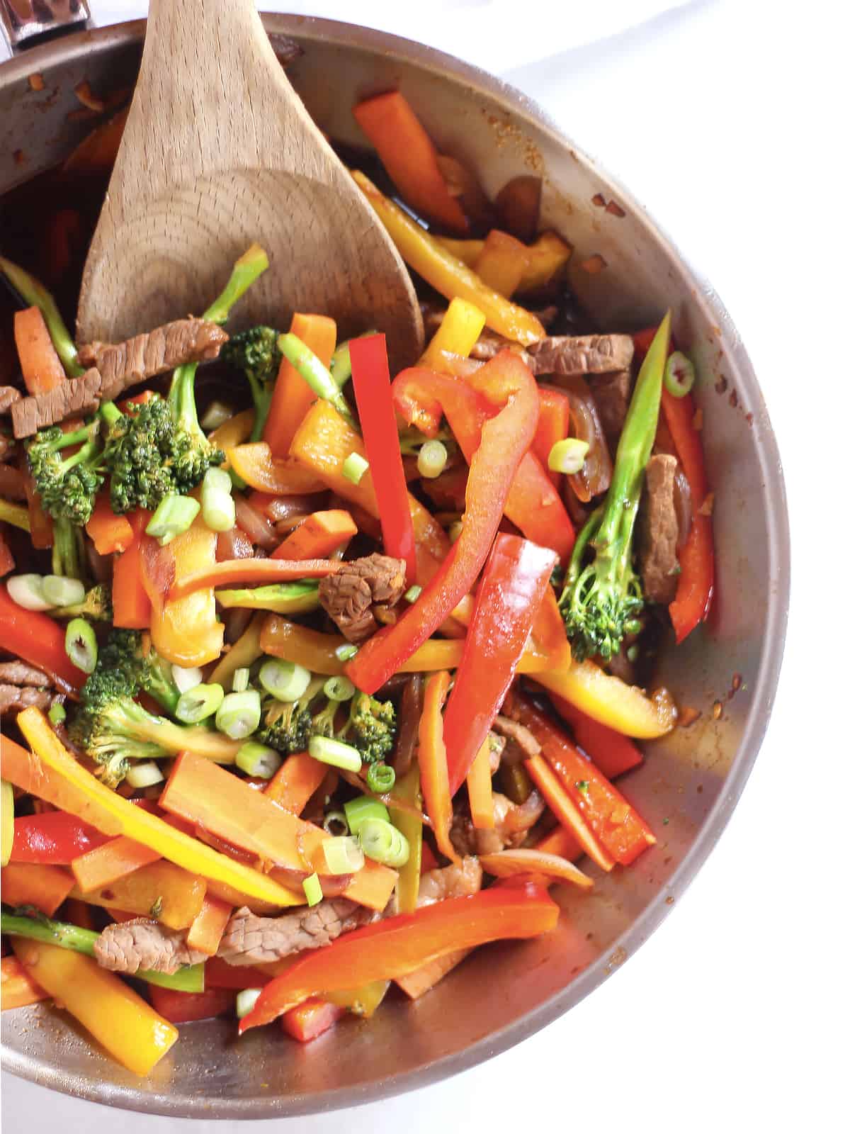 Strips of beef and julienne vegetables in a skillet with a wooden spoon.