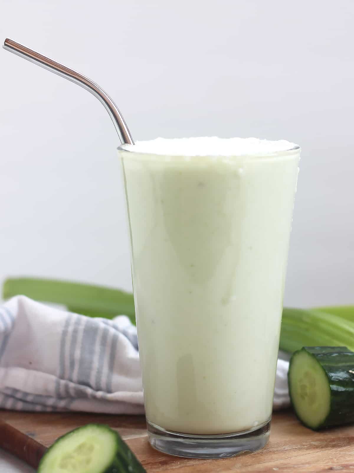 A celery cucumber and apple smoothie in a glass with a metal straw.