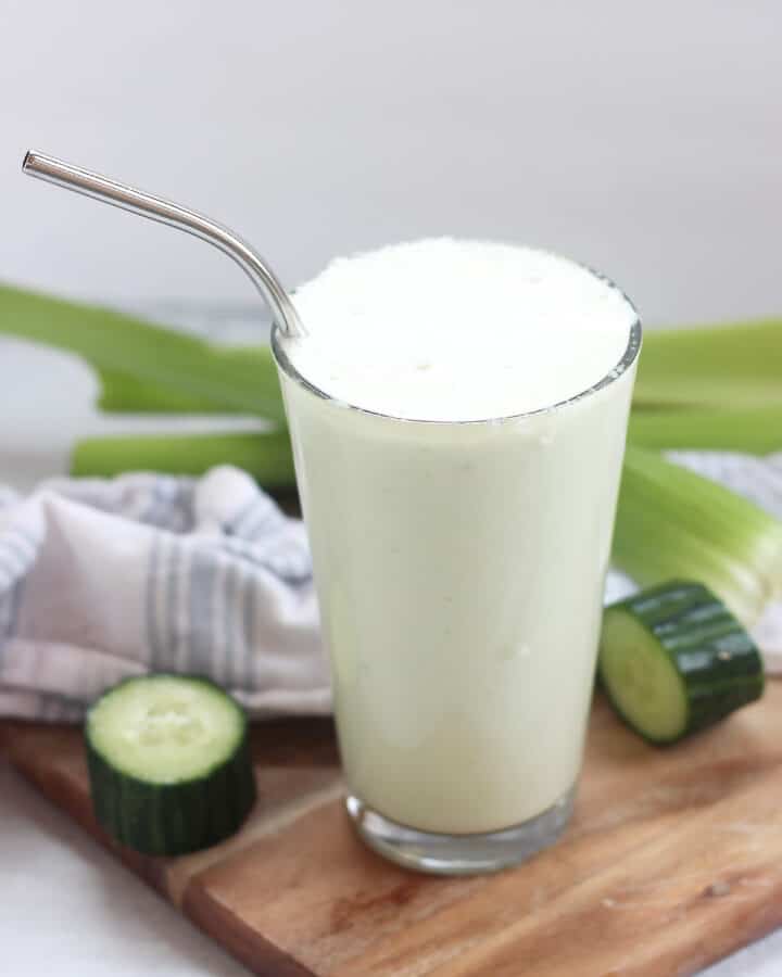 A celery cucumber apple smoothie poured into a tall glass with a straw.