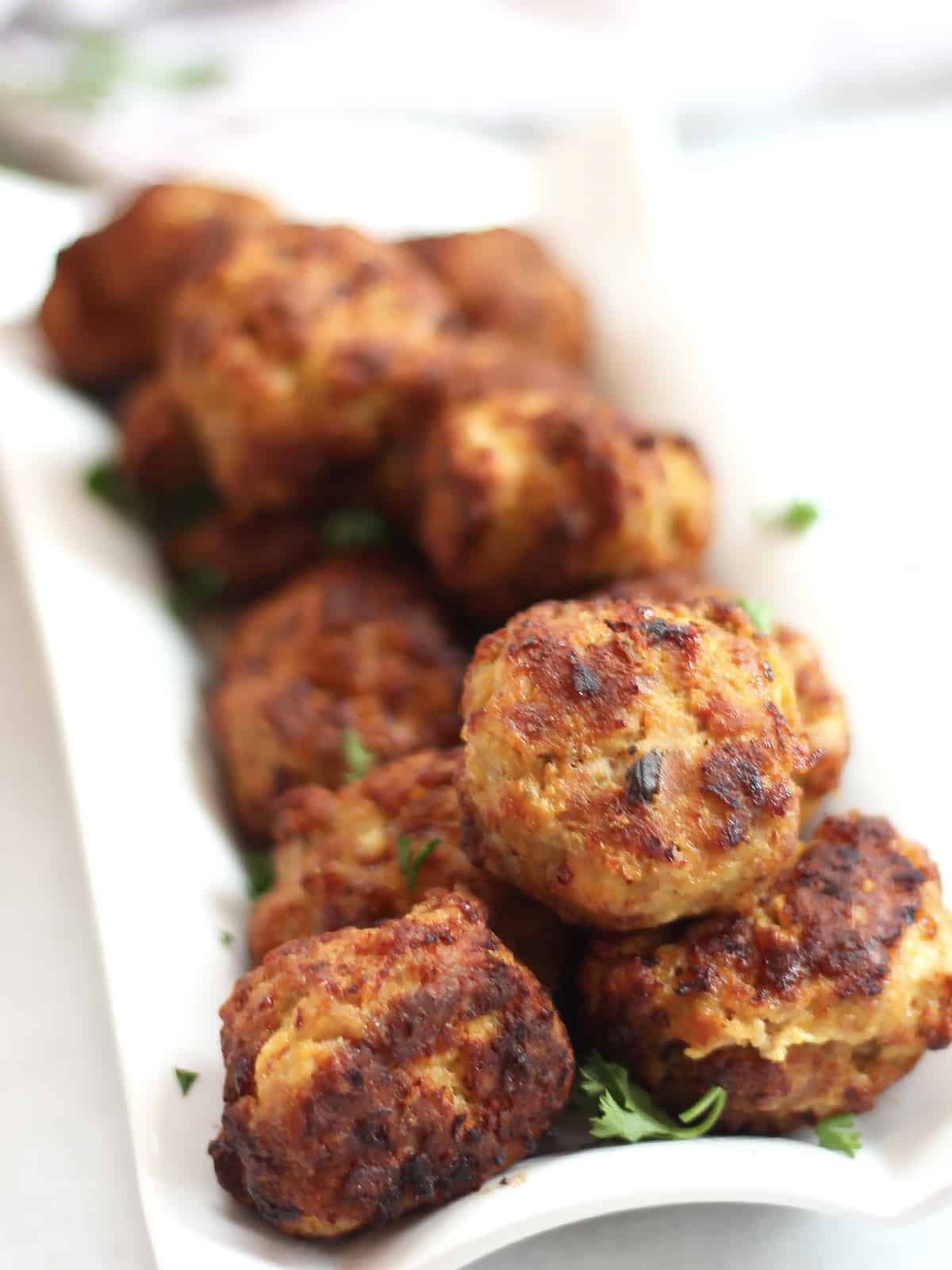 Air fried meatballs on a white plate garnished with fresh parsley.