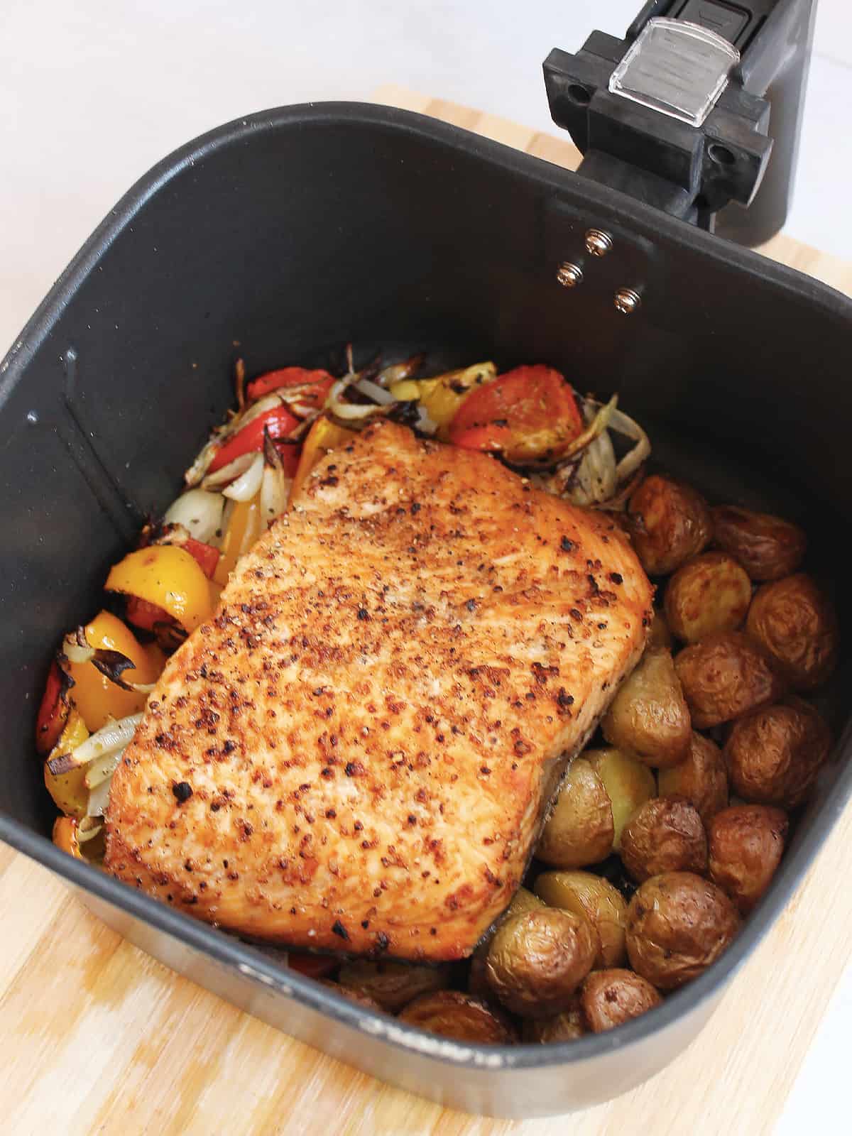 Salmon fillet, vegetables and potatoes in an air fryer basket ready to serve.