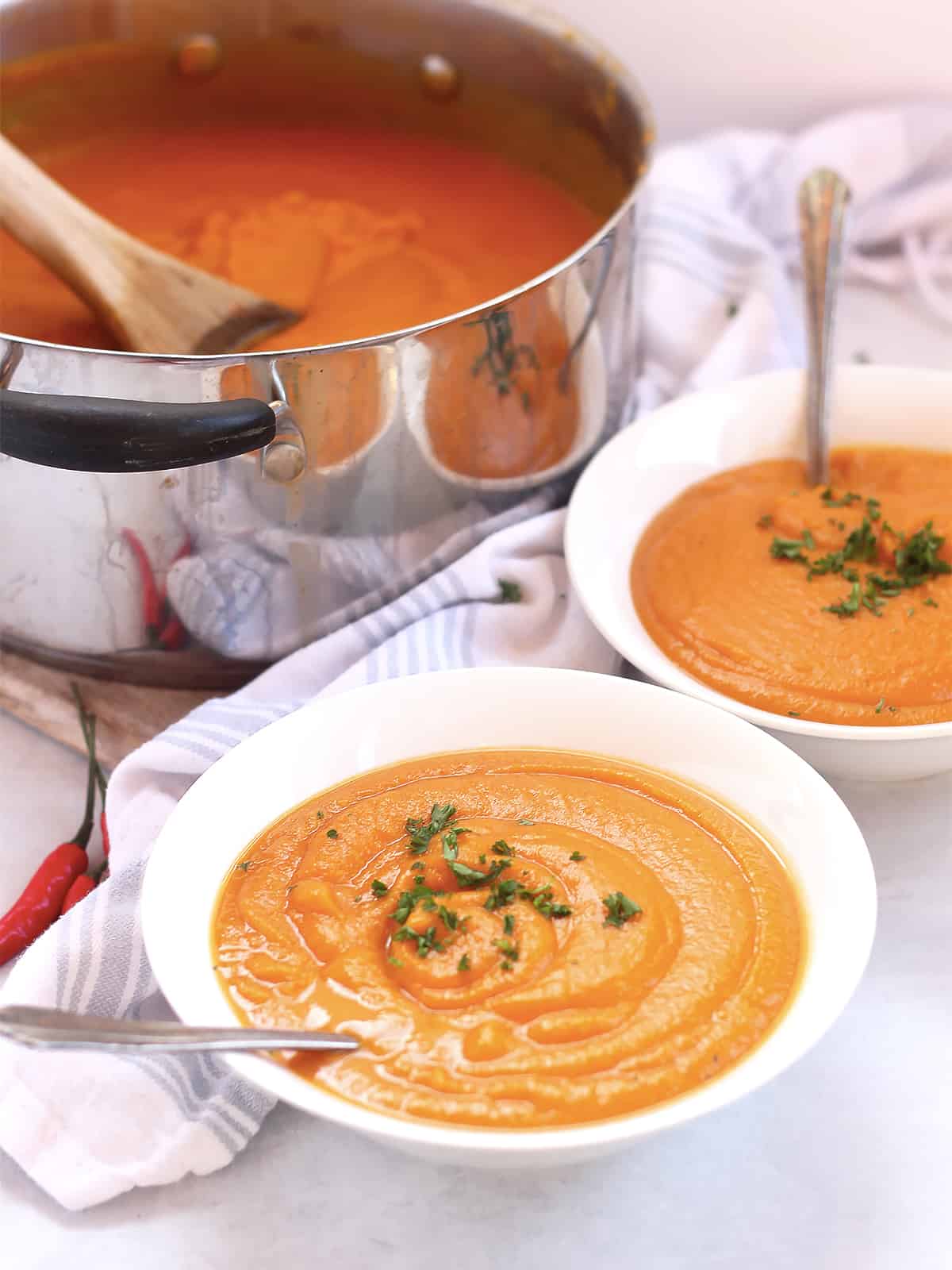 Two bowls of soup served from a large silver pot.