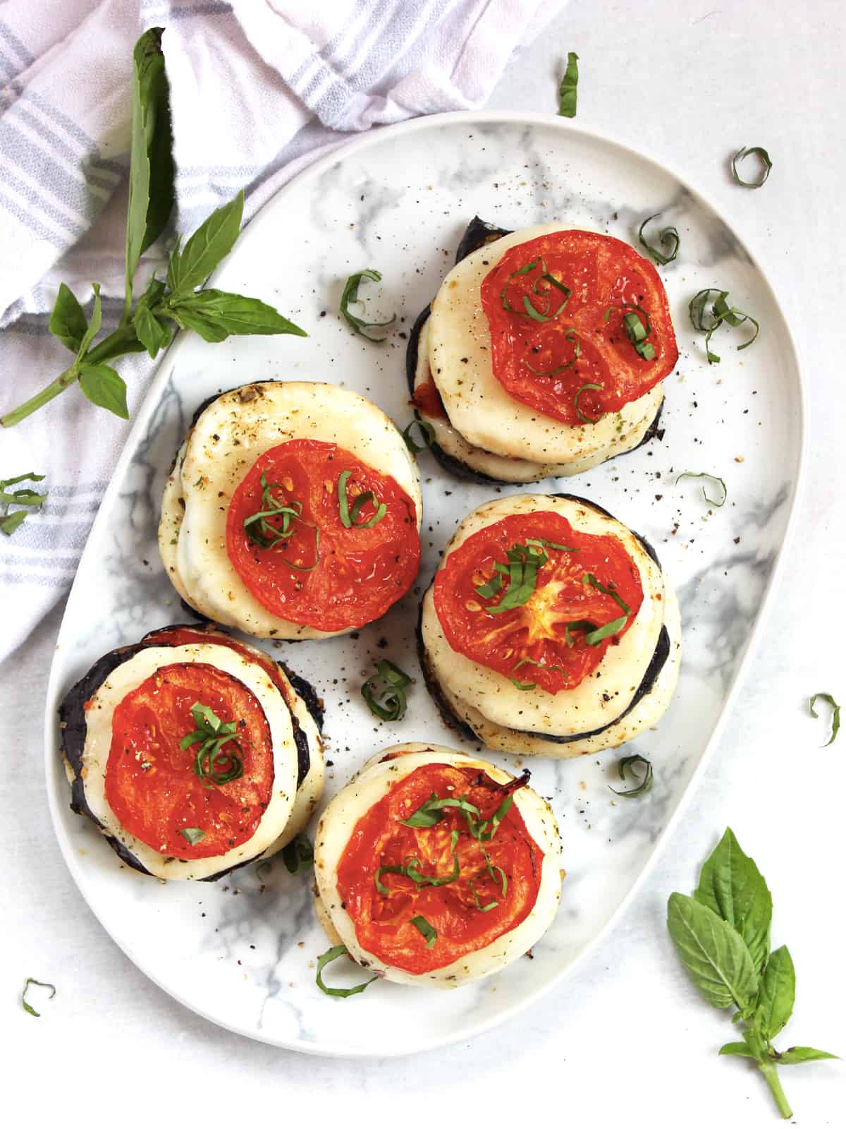 Five eggplant mozzarella stacks topped with sliced roasted tomatoes.