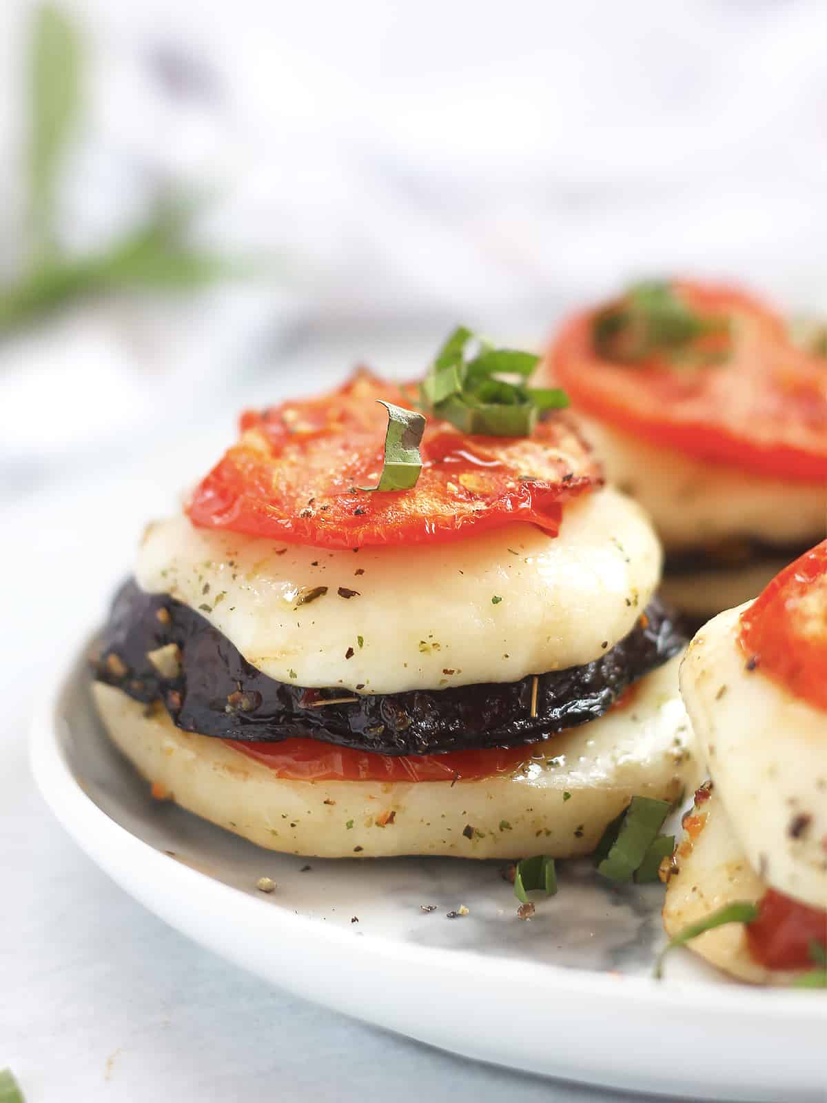 Sliced eggplant, tomato and mozzarella stacked on top of each other and garnished with fresh basil.