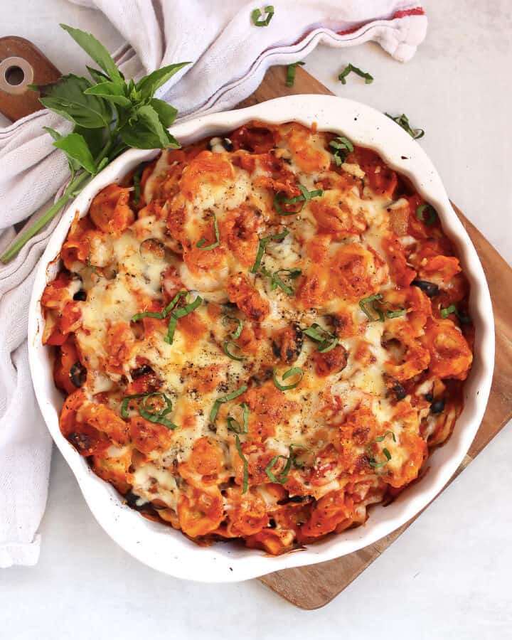 Baked tortellini and vegetables in a white baking dish, garnished with fresh basil.