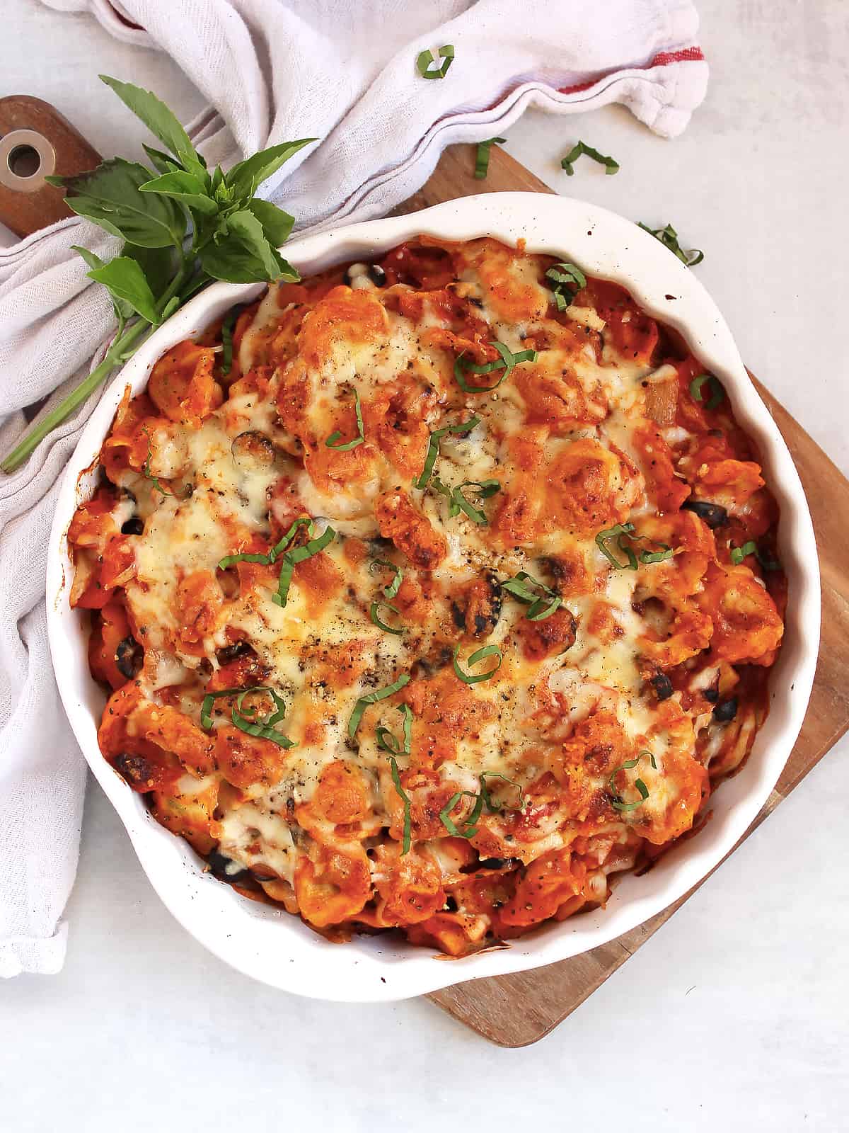 Baked tortellini and vegetables in a white baking dish, garnished with fresh basil.