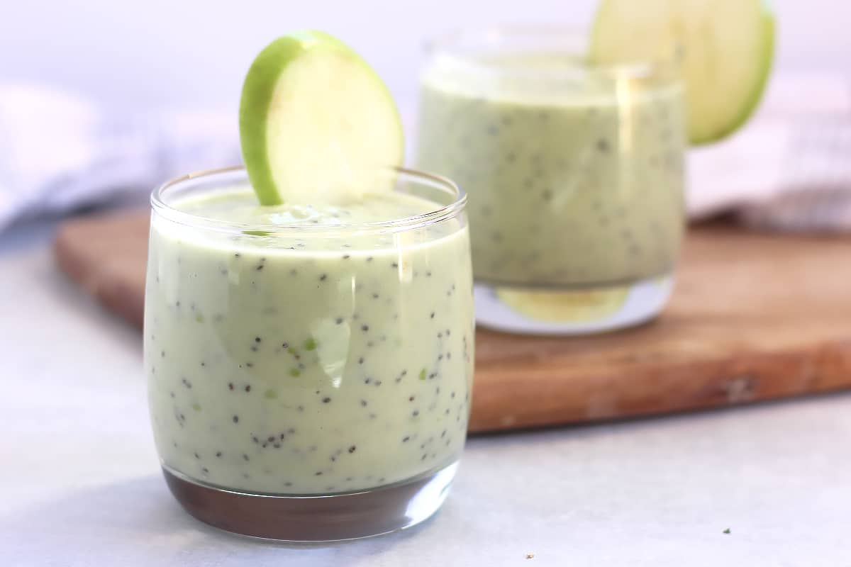 Green smoothie with chia seeds served in two glasses with fresh apple slices.