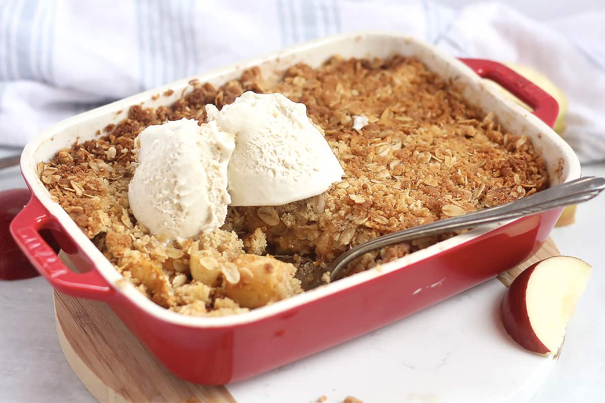 Air fried apple crisp in a red baking dish with a serving spoon.
