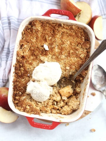 Air fryer apple crisp in a baking dish with a serving spoon and topped with ice cream.