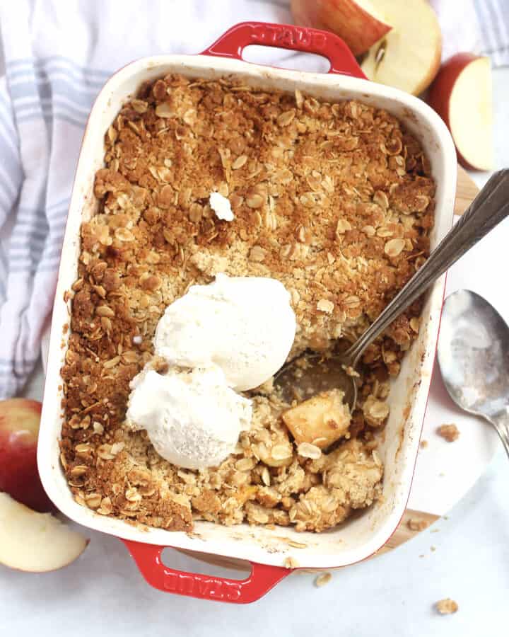 Air fryer apple crisp in a baking dish with a serving spoon and topped with ice cream.