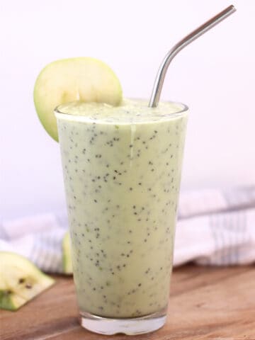 An apple avocado smoothie served in a tall glass with a silver straw.