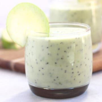 Green smoothie in a glass garnished with an apple slice.