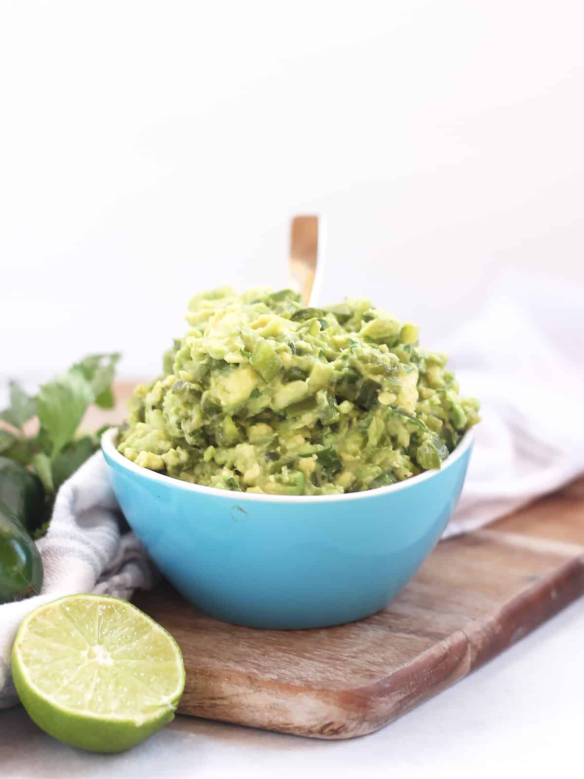 A bowl of guacamole on a wooden chopping board.