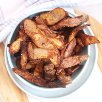 Air fried potato peeling chips in a blue bowl.
