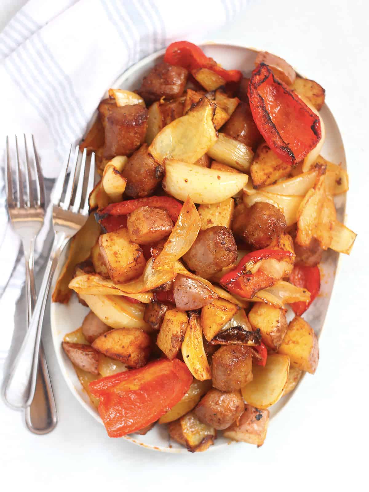 Air fryer sausage, peppers, onions and potatoes on a serving plate next to two forks.