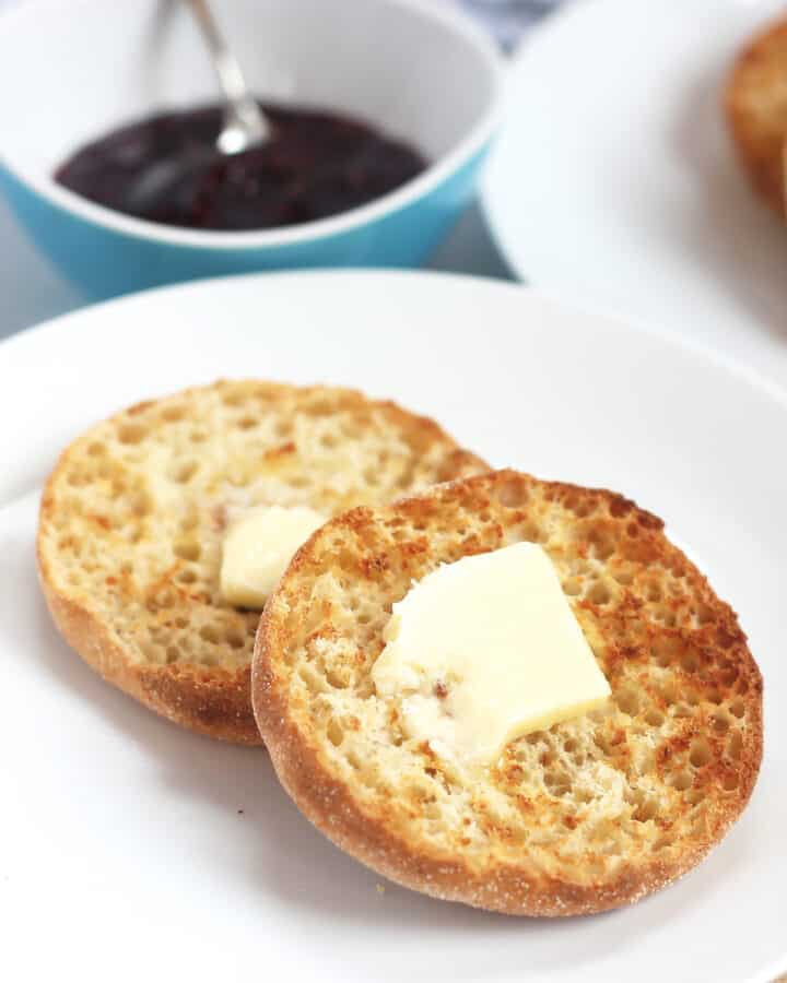 Air fried English muffin halves with butter next to w bowl of jam.