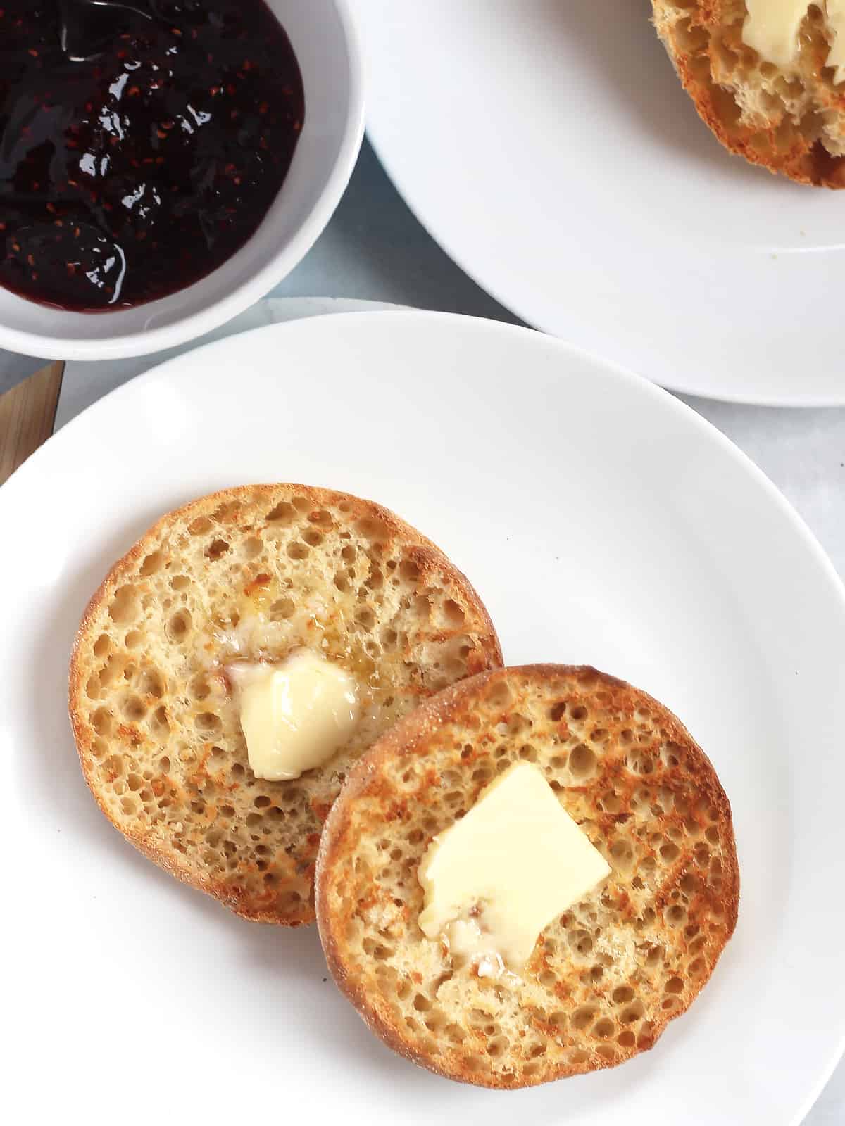 Two air fried English muffin halves with butter, next to a bowl of jam.