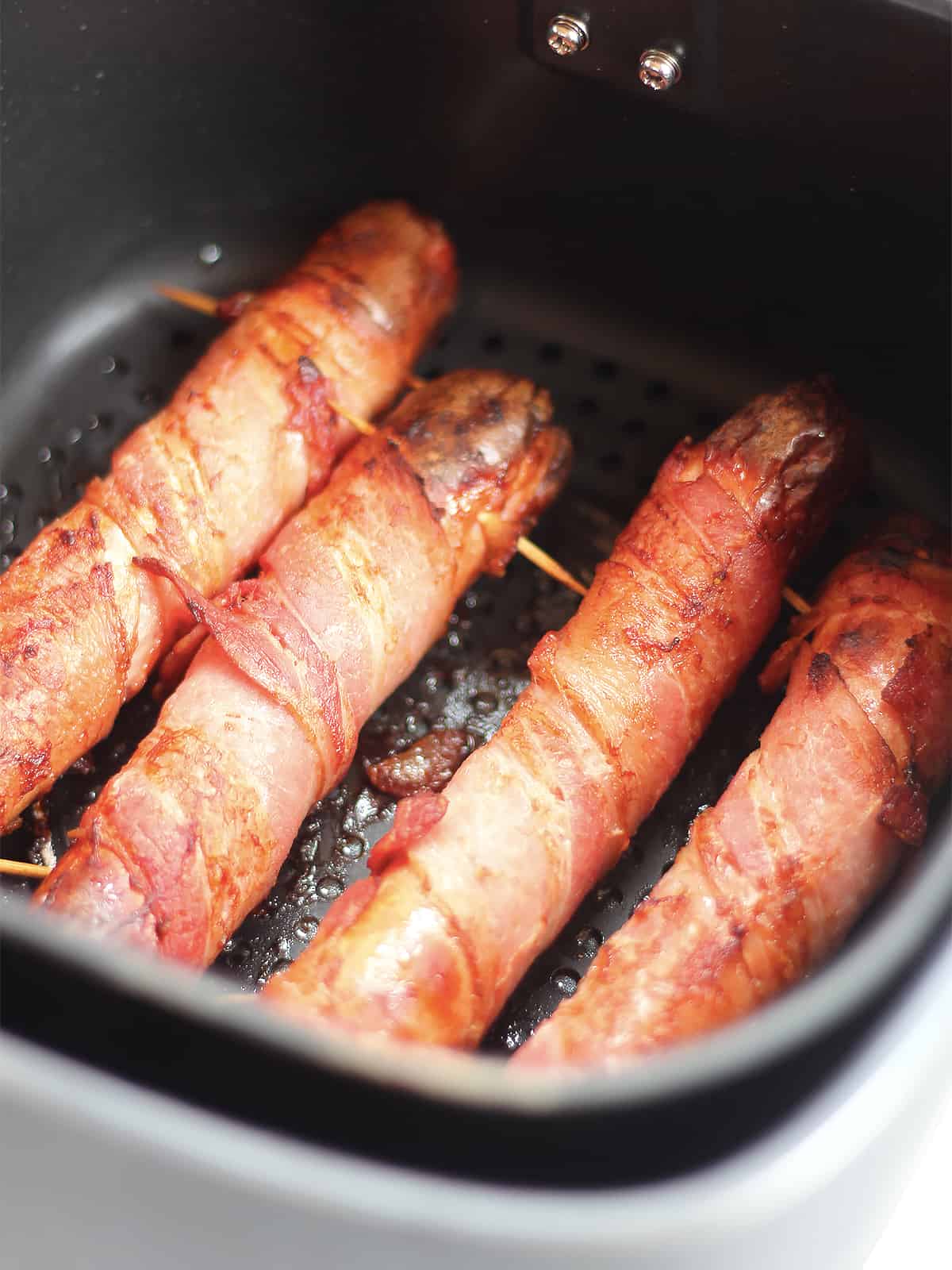 Air fried bacon wrapped hotdogs in the air fryer basket.