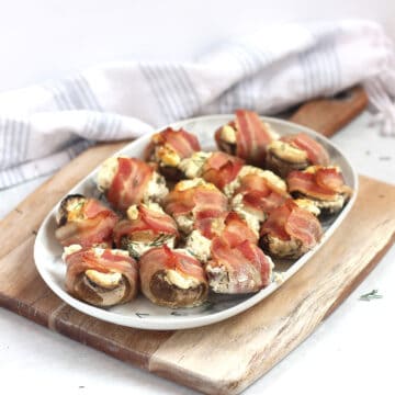 A plate of bacon wrapped mushrooms on a wooden chopping board.