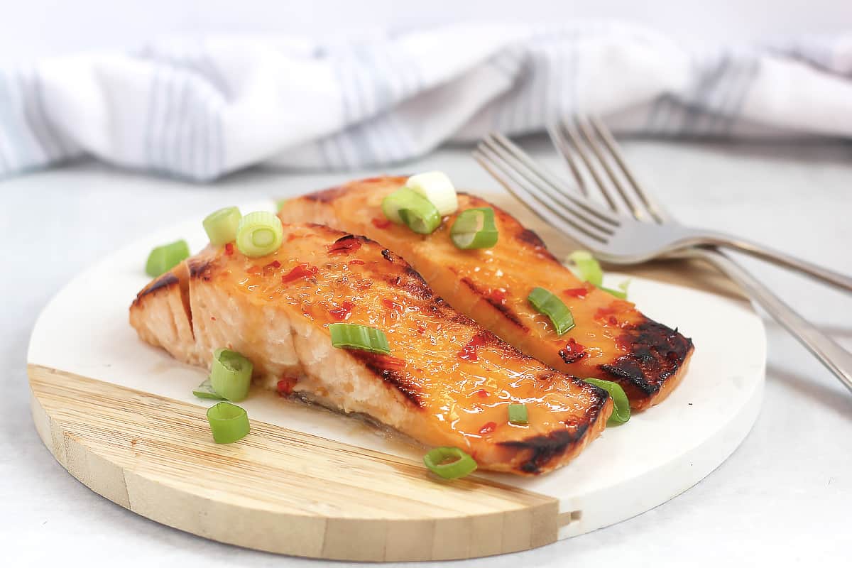 Sweet chili glazed salmon fillets next to two forks on a wooden chopping board.