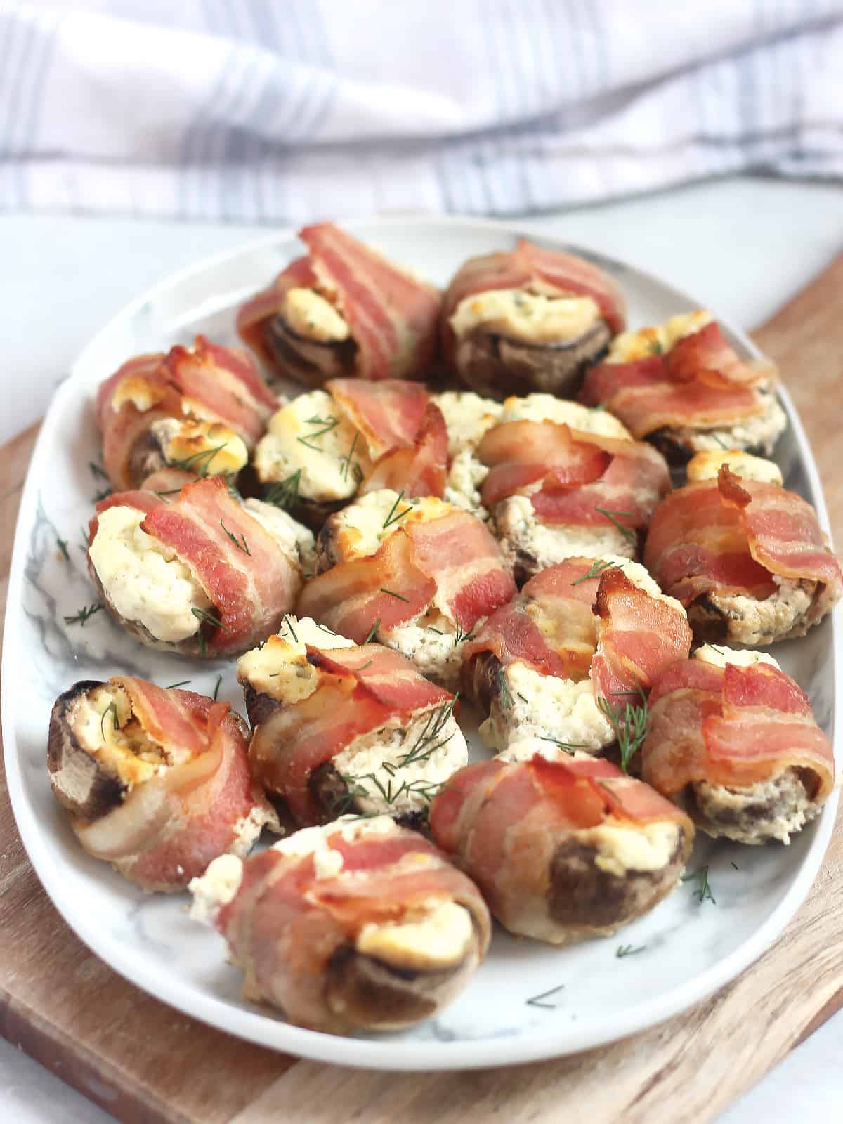 Boursin stuffed mushrooms wrapped with bacon on a serving plate.