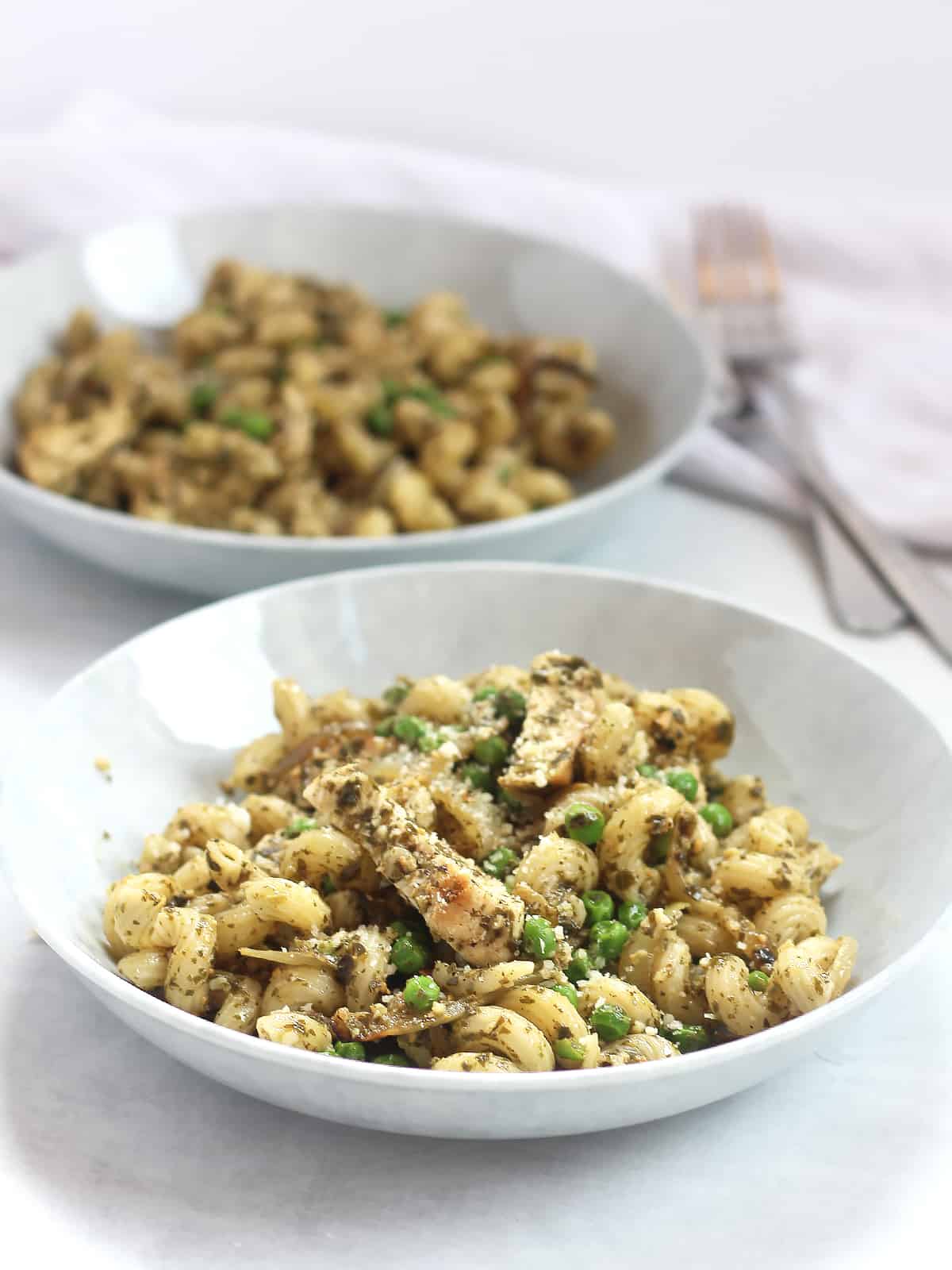 Two bowls of pasta with chicken, pesto and peas.