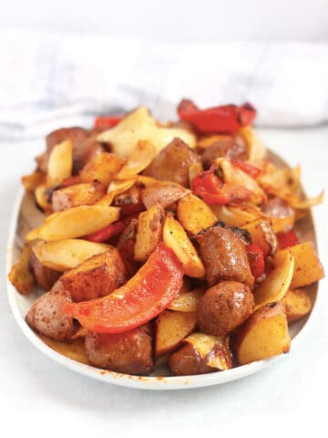 Cooked sausage, peppers, onions and potatoes served on a large plate.