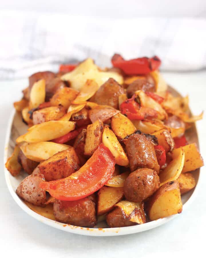 Cooked sausage, peppers, onions and potatoes served on a large plate.