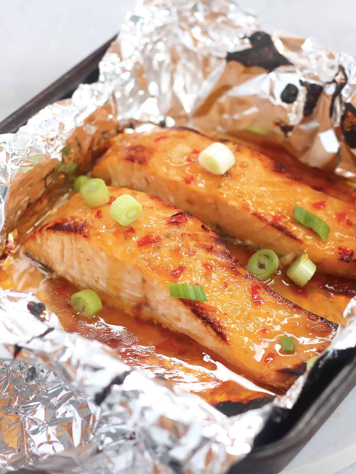 Two sweet chili salmon fillets in a foil lined tin, garnished with sliced green onions.