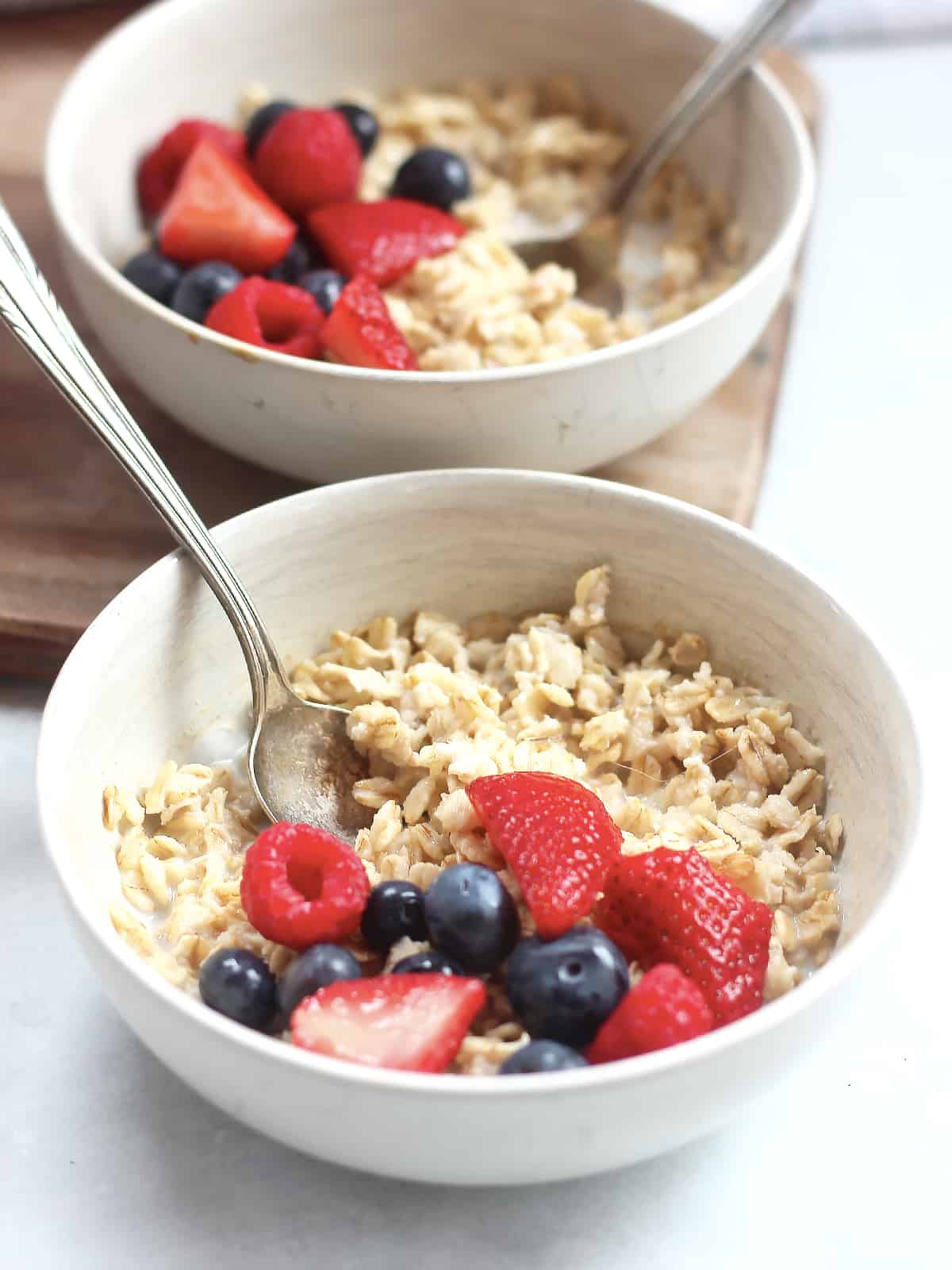 Two bowls of oatmeal with spoons in.