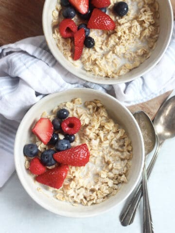 Two bowls of air fryer oatmeal topped with fresh berries, next to two spoons.