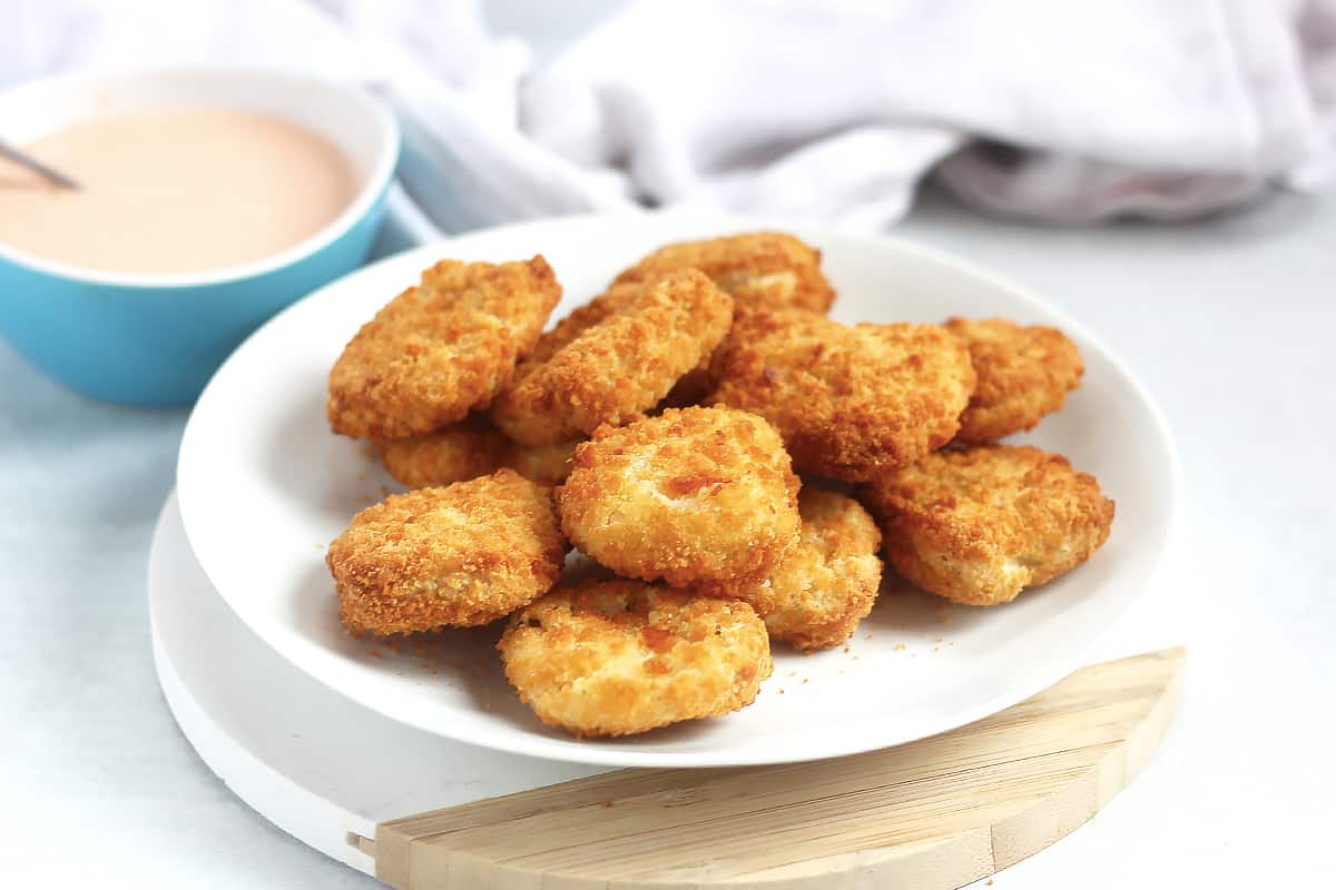 Air fryer chicken nuggets on a plate next to a bowl of dipping sauce.