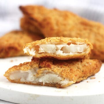 A piece of breaded fish cut in half so that you can see the flaky white flesh.